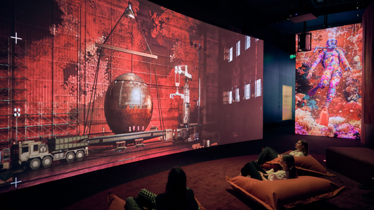 People sit on large cushions watching a futuristic projection at ACMI