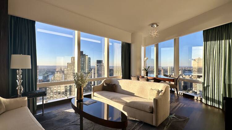 A hotel suite with couches and a table in front of skyline views.