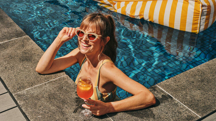 A woman in a pool with an Aperol Spritz.