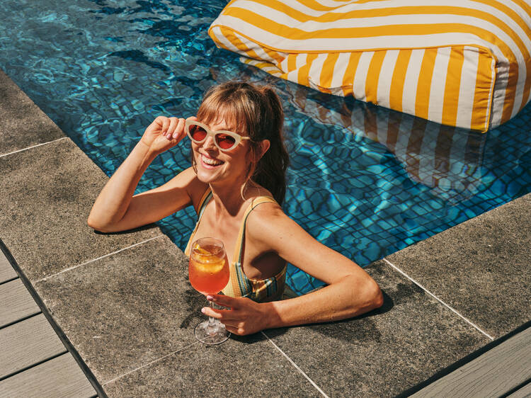 A woman in a pool with an Aperol Spritz.