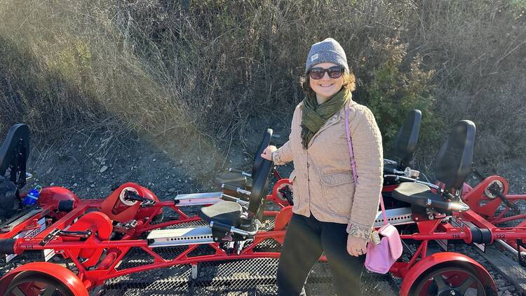 A woman stands next to a red rail explorers bike.