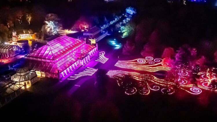 An aerial shot of Christmas at Kew, showing the Temperate House illuminated in pink, and swirling red carpets of light leading up to it 