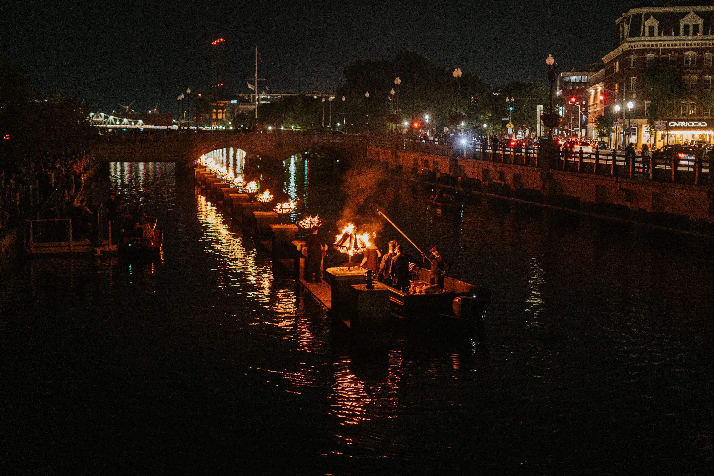 People on a boat light up braziers in a river.