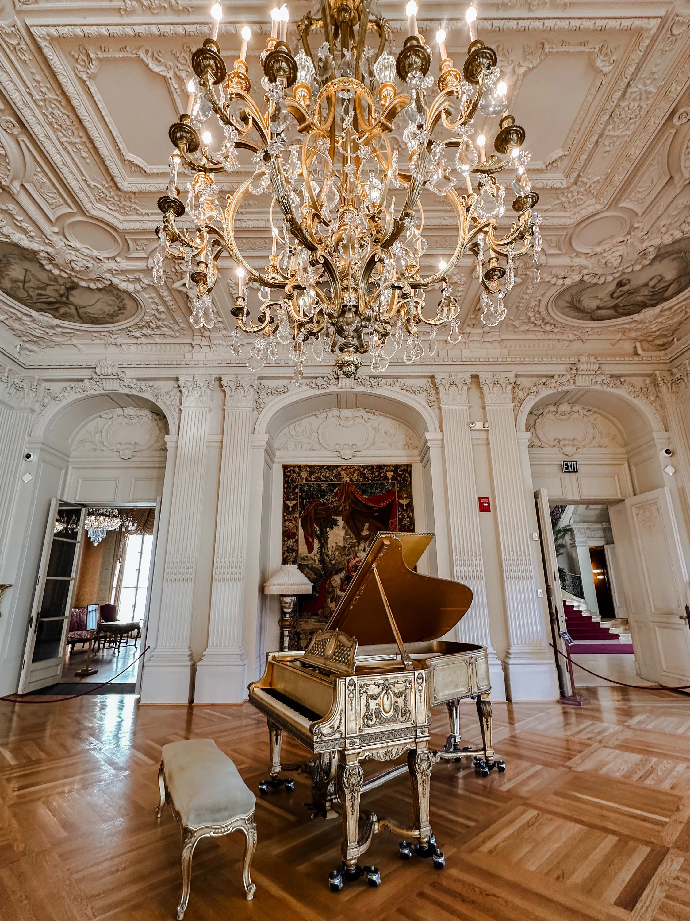 A chandelier and piano inside a fancy mansion.