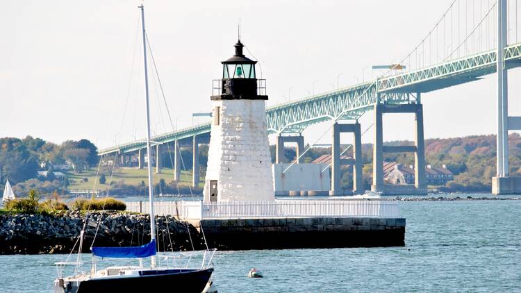 A boat and lighthouse in front of a bridge.