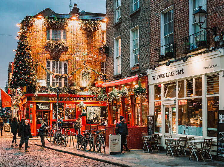 Dublin, Ireland - November 8, 2018: Famous Temple Bar. Christmas tree, illumination and decorations above entrance. Vintage terrace with empty coffee table. Cozy alley view in autumn. Lifestyles.