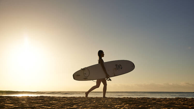 Woman heading out for a morning surf at Avoca Beach on the Central Coast.