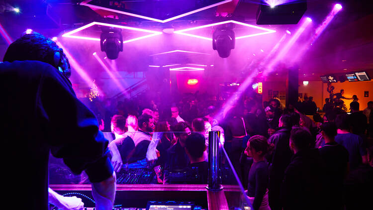 A crowd dances illuminated by purple lights viewed from the DJ booth at Rowan’s