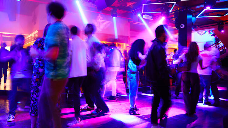 A crowd of people on a wooden dance floor illuminated by blue and purple strobe lighting 