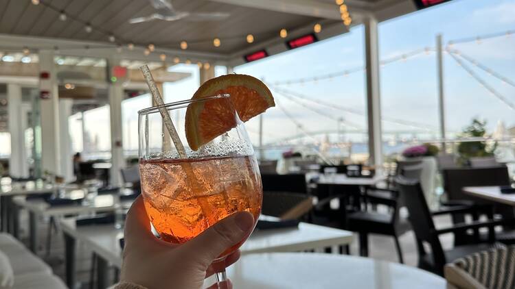 A hang holds up an aperol spritz cocktail on a hotel patio bar.