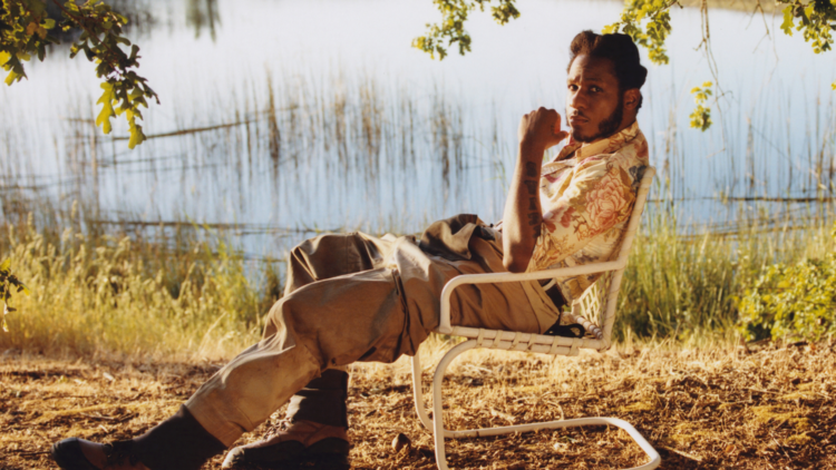 Leon Bridges sitting in a chair by a lake