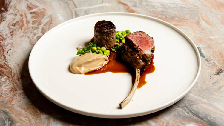 Rack of meat on white plate with sauce and green peas