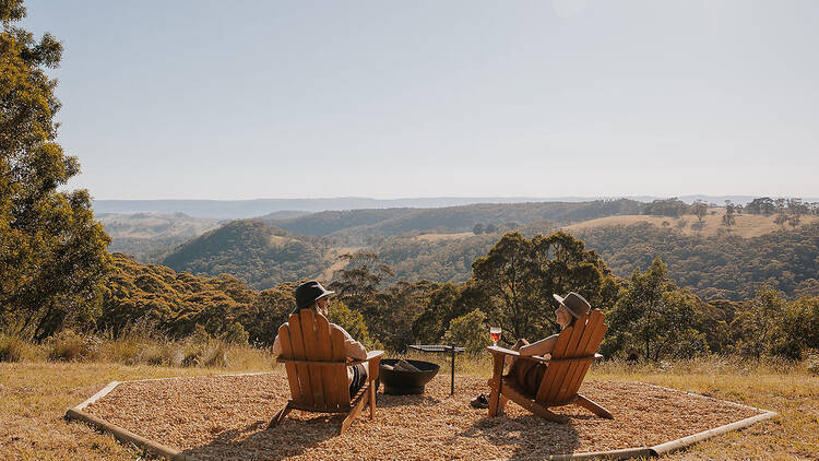 Two people sitting on deck chairs looking out over bush