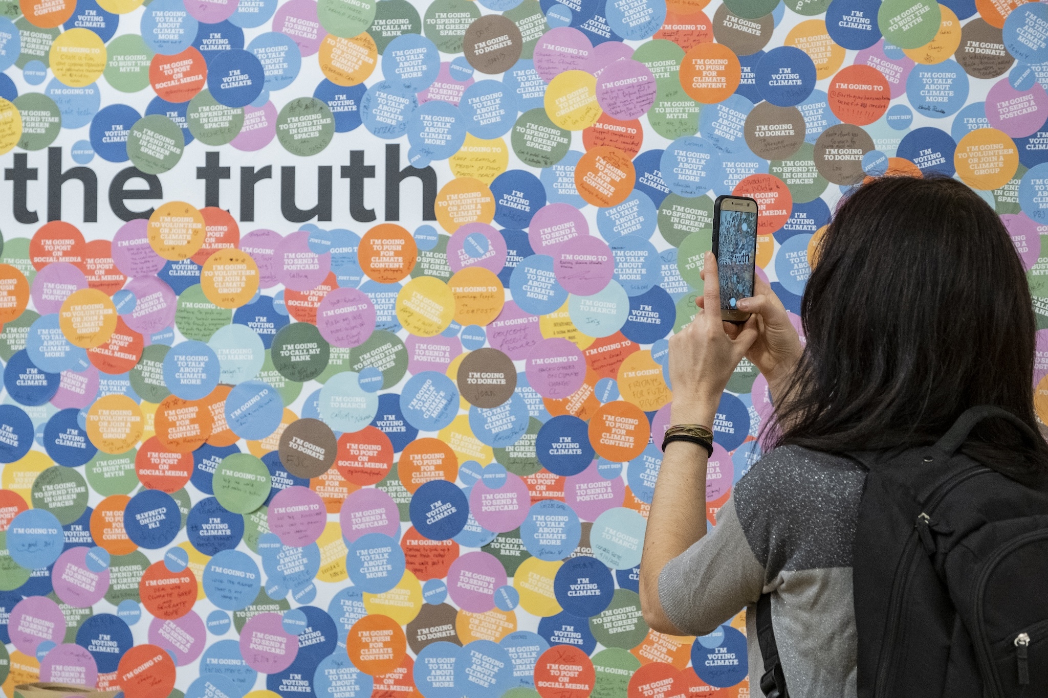 A woman takes a photo of a colorful wall reading "The Truth." 