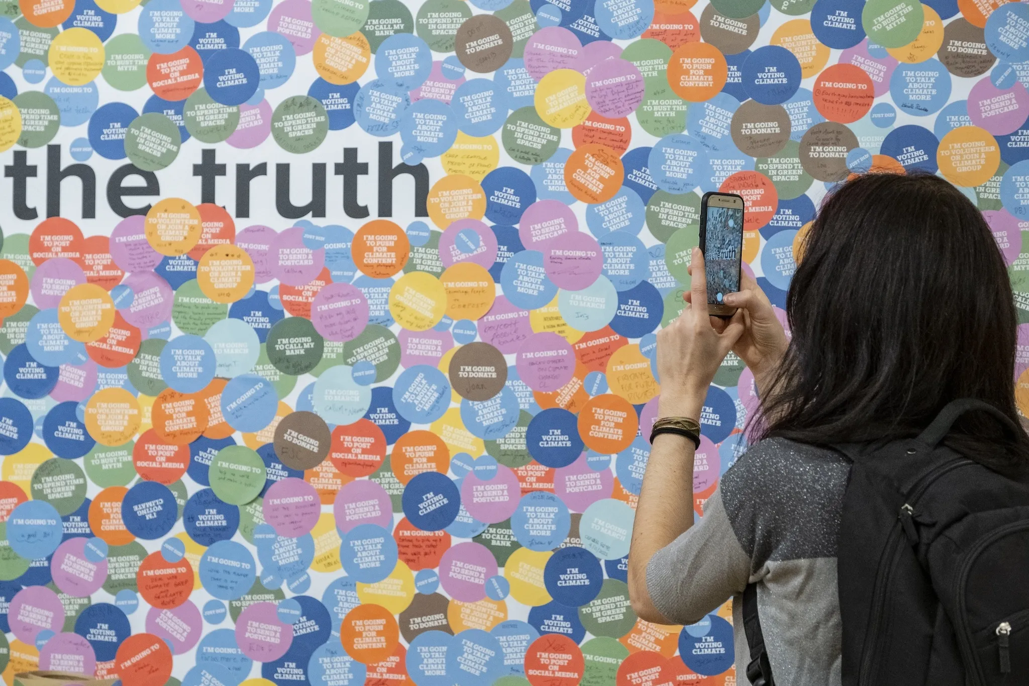 A woman takes a photo of a colorful wall reading "The Truth."