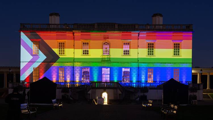 A night-time view of the exterior of Queen’s House illuminated by the LGBTQ+ flag