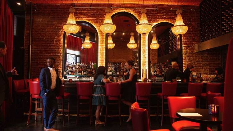 People stand at a large bar beneath chandeliers.