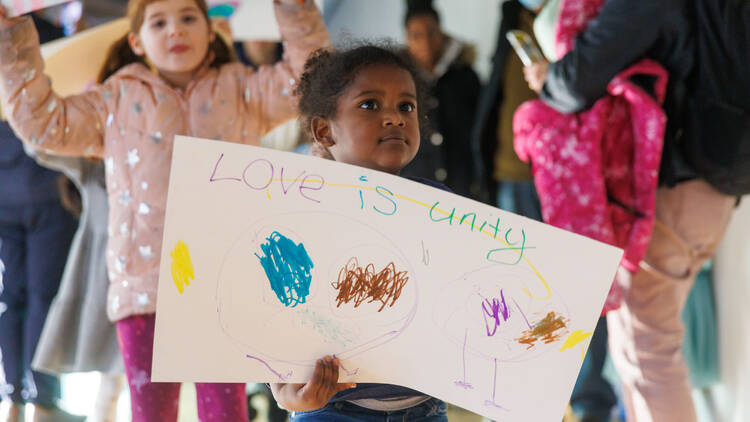 A child holds a hand-drawn sign reading Love Is Unity.