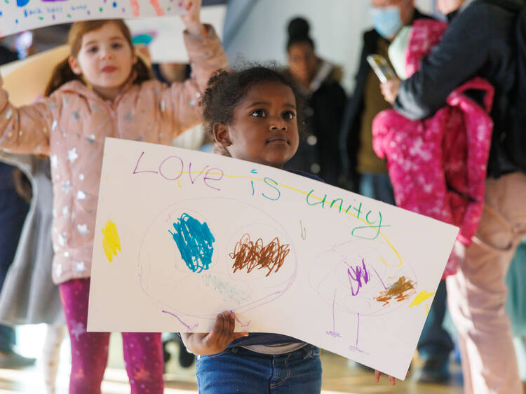 A child holds a hand-drawn sign reading Love Is Unity.