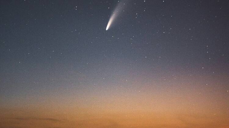 A comet streaking through a night sky at sunset.