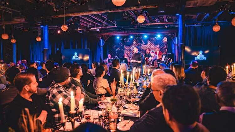 People gather around tables at a candlelit dinner show.