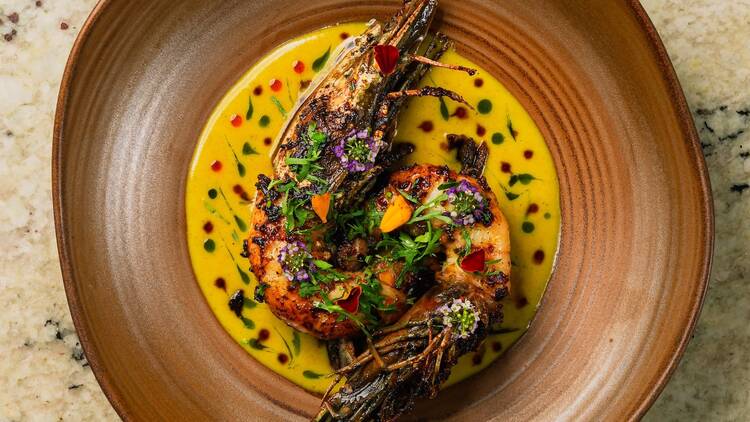 A brown plate with prawns in a yellow curry