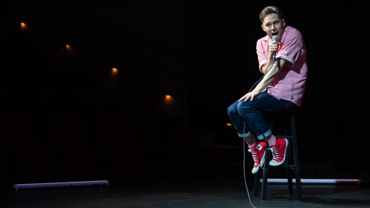 Samuel Barnett on-stage sitting on a stool