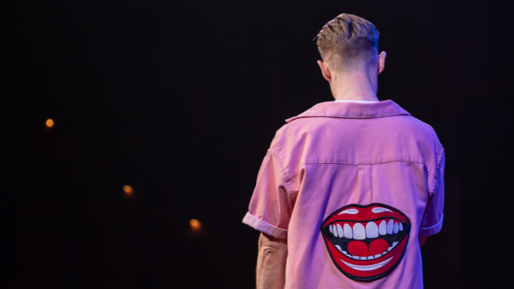 Samuel Barnett seen from the back wearing a shirt with an open mouth on it