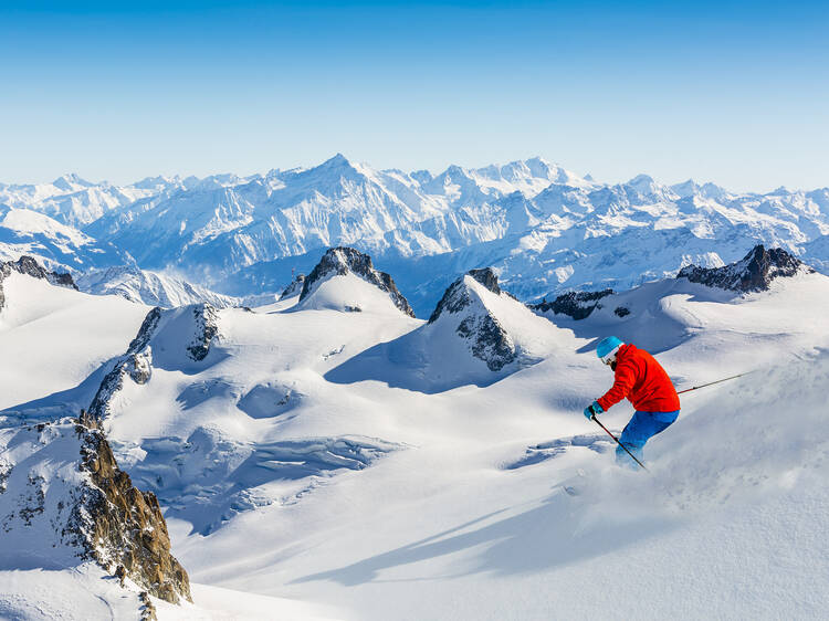 Skier skiing downhill Valle Blanche in french Alps in fresh powder snow. Snow mountain range Mont Blanc with Grand Jorasses in background.