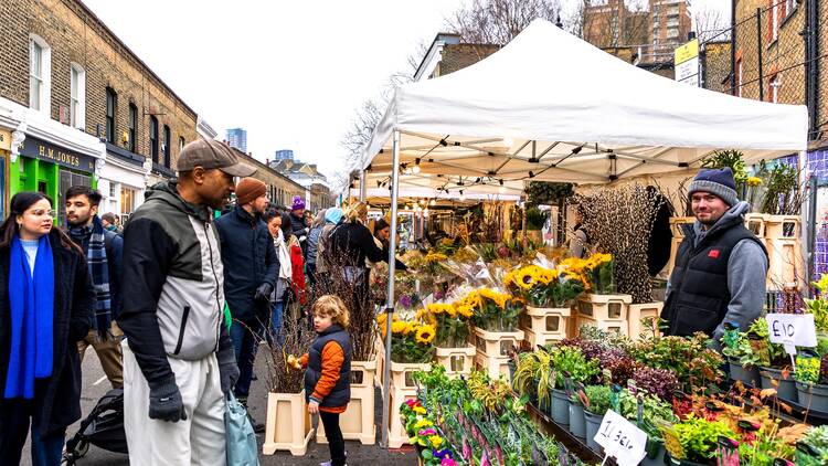 A man inspects rows of flower bunches sitting in buckets of water on a stall at Columbia Road Flower Market