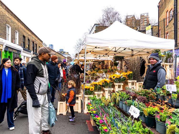 A man inspects rows of flower bunches sitting in buckets of water on a stall at Columbia Road Flower Market