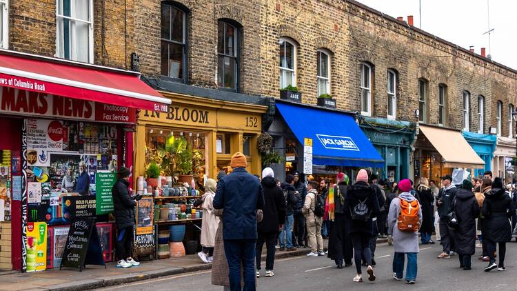 Crowds of people walking past a row of brightly coloured shopfronts on Columbia Road