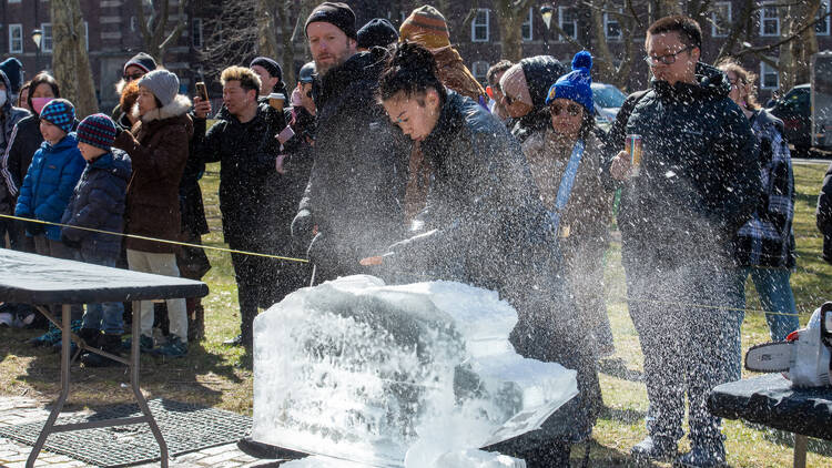 A woman carves a block of ice, spraying icy dust into the air.