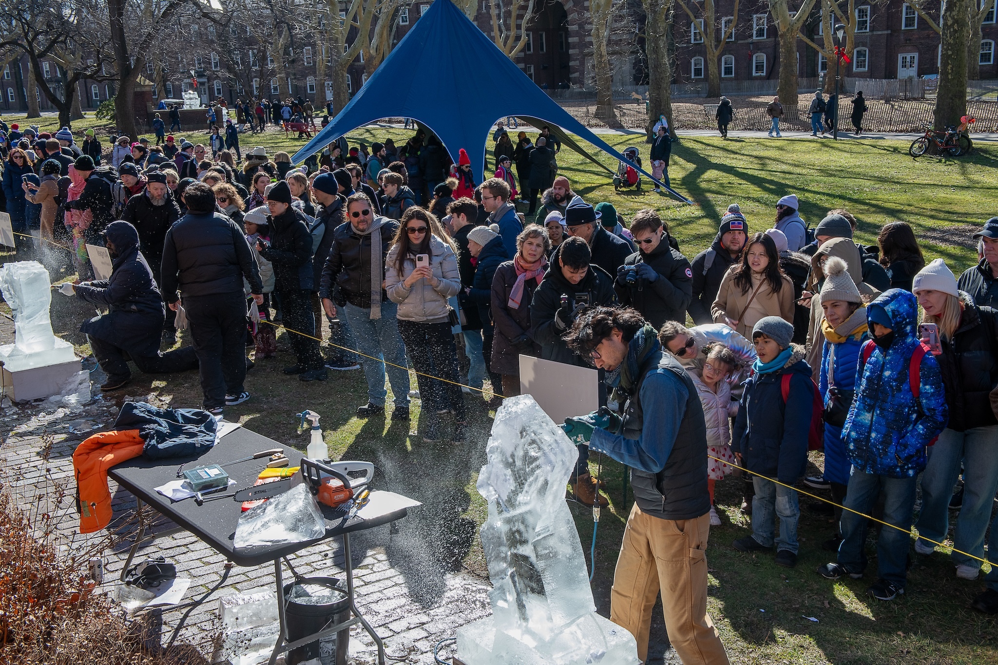 A person carves a block of ice as a large crowd watches.