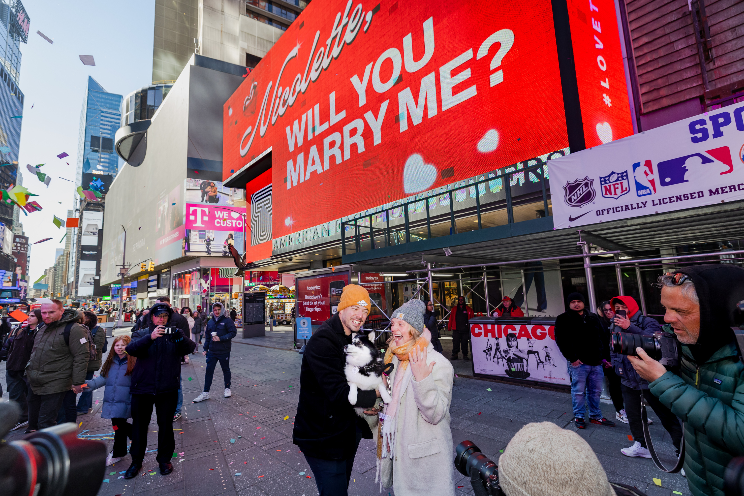 A couple gets engaged in Times Square in front of a large billboard saying, "Will you marry me?"