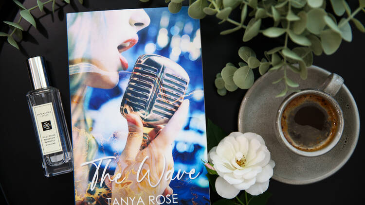 A book laying on a table with coffee and perfume