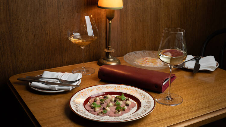 A dining table with two glasses of wine and a plate of food at Bar Olo.