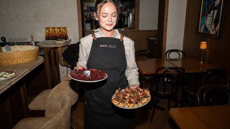 A waiter walking through Bar Olo with two plates of food.