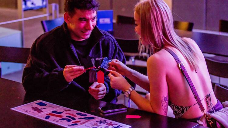 Two people sitting at a table holding paper butterflies. 