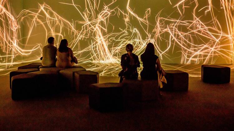 People sitting in front of a large projection of strings of light.