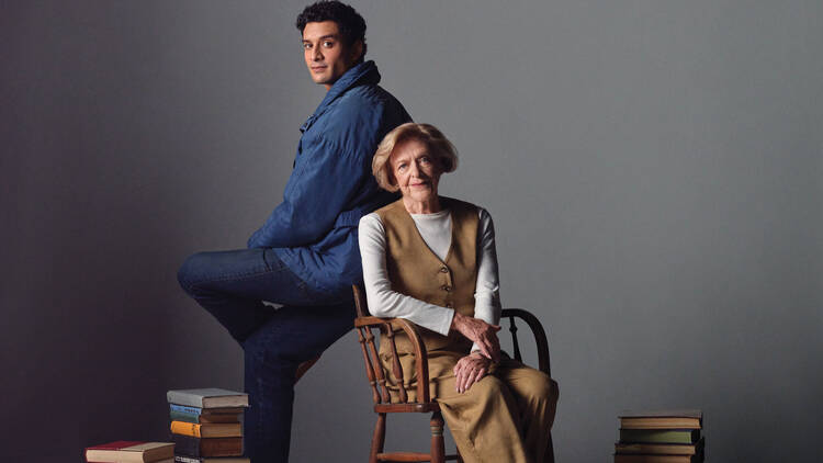 A younger man and older woman posing for a photo surrounded by books