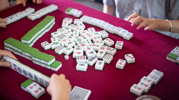 People playing mahjong traditional Chinese board game on a red table at home. 