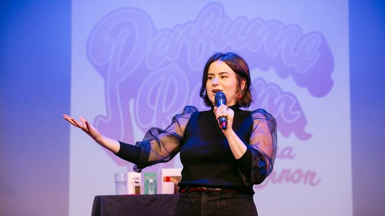 A woman on stage in front of a logo reading Perfume Room.