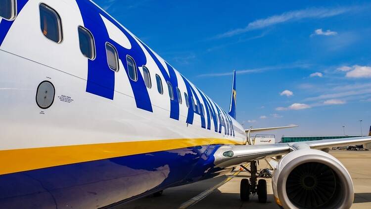 Ryanair aircraft shot from the side looking back towards the wings and tail, blue sky with dotted white clouds. 