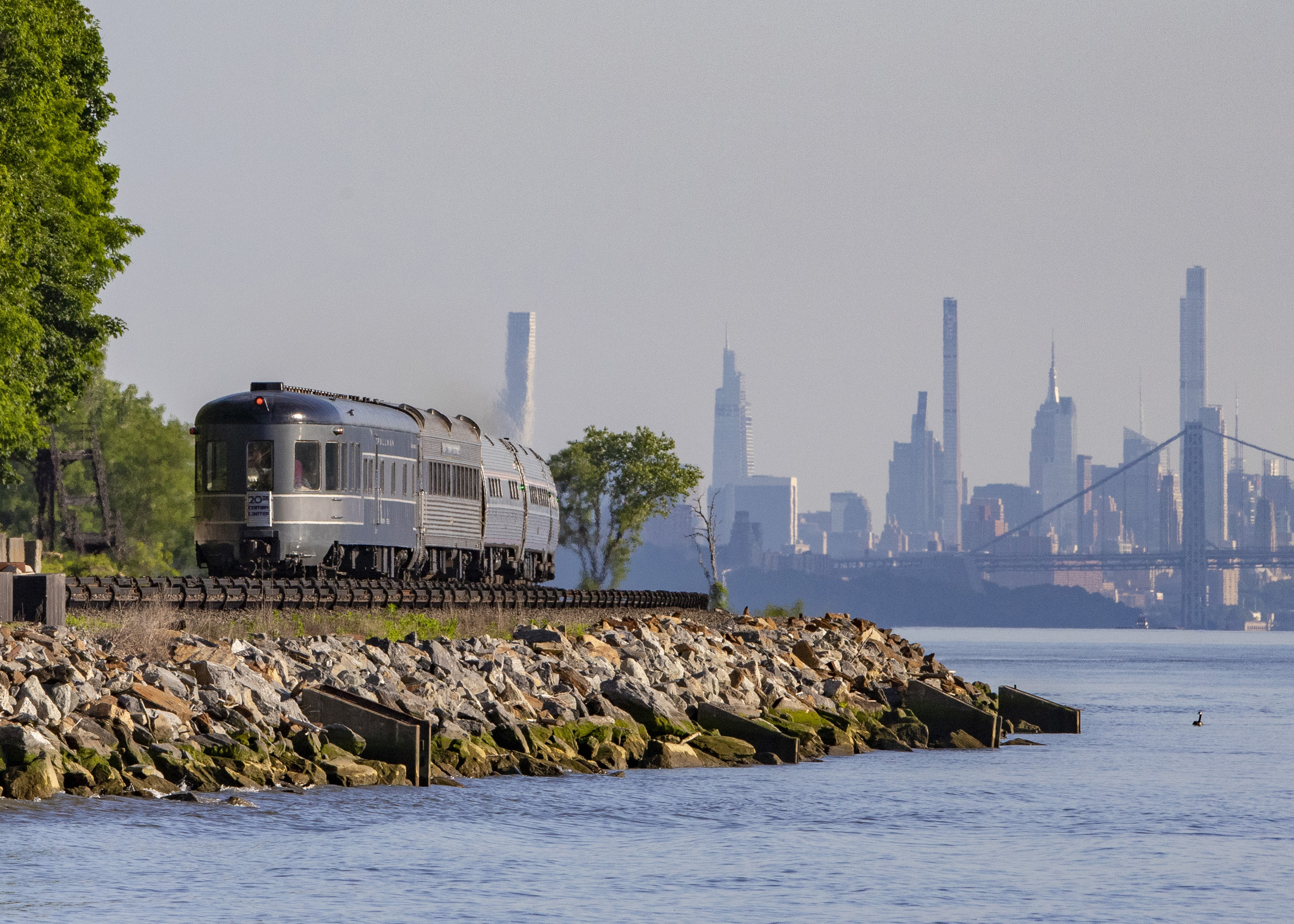 An old train car rides along the Hudson with the NYC skyline in the background.