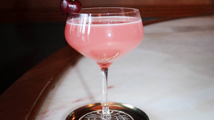 A pink cocktail in a glass with a cherry garnish.