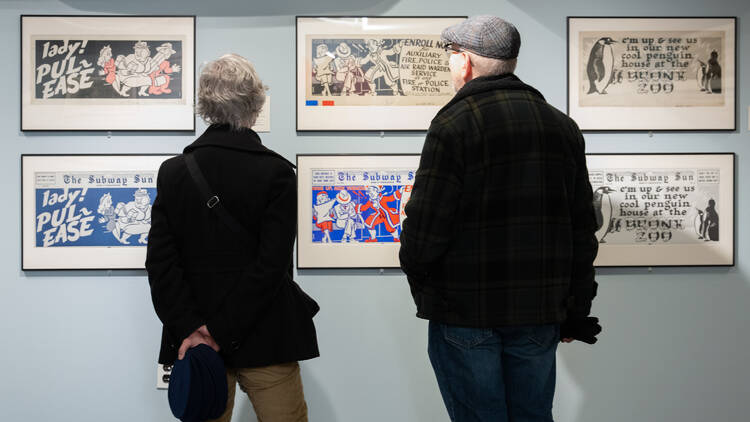 Two people look at ads in a subway exhibit.