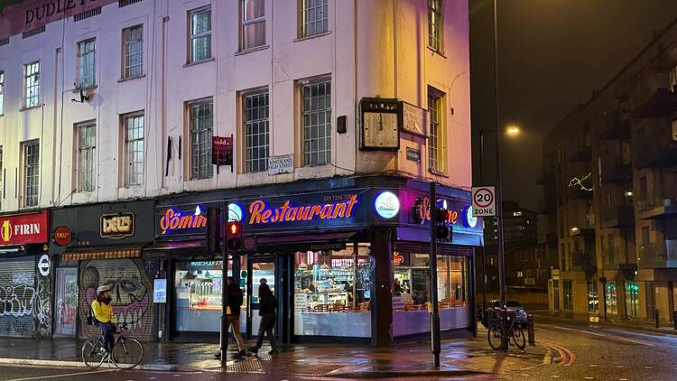 Exterior of a restaurant at night, viewed from across the street corner; its name Sömine Restaurant is illuminated in orange neon