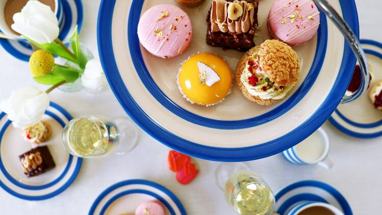 A series of blue and white plates filled with cakes and scones sitting on a white tablecloth