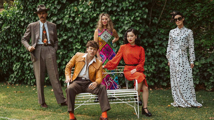 Five people dressed in vintage clothing pose in a garden.